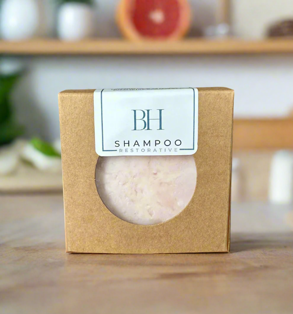 Shampoo bar in a brown box with 'BH' label on a wooden surface with a fruit and plant in the background